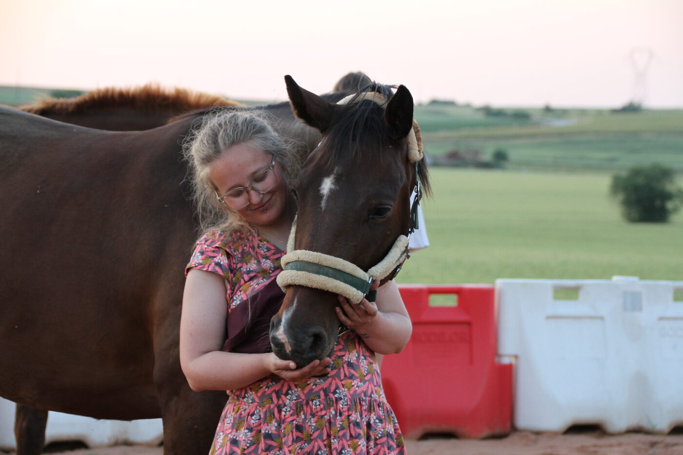Cellia et un cheval bai partagent un moment de tendresse en fin de journée